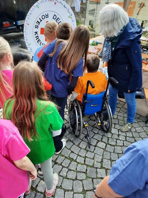 Auf dem Foto sind verschiedene Mensch, vor allen Dingen Kinder, von hinten zu sehen. Ein Kind sitzt im Rollstuhl. Sie stehen an für ein Glücksspiel an einem Glücksrad, welches die Wendlandschule in Dannenberg am 8. Mai angeboten hatten.