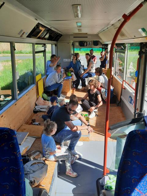 Auf dem Bild ist eine größere Gruppen von Erwachsenen und Kindern in dem alten Bus "Bernhard" zu sehen. Die Kinder und manche Erwachsene sitzen am Boden, manche sitzen, manche stehen.