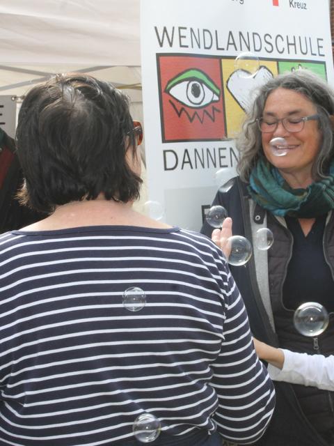 Auf dem Bild sind zwei Personen zu sehen an dem Stand von der Wendlandschule in Dannenberg. In dem Bild sind auch Seifenblasen zu sehen.