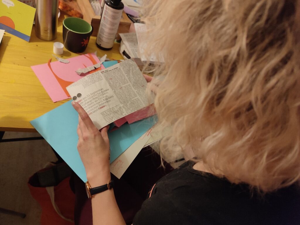 Im Vordergrund ist das blonde Haar einer Teilnehmerin. Sie hält Bastelmaterial in ihrer Hand.