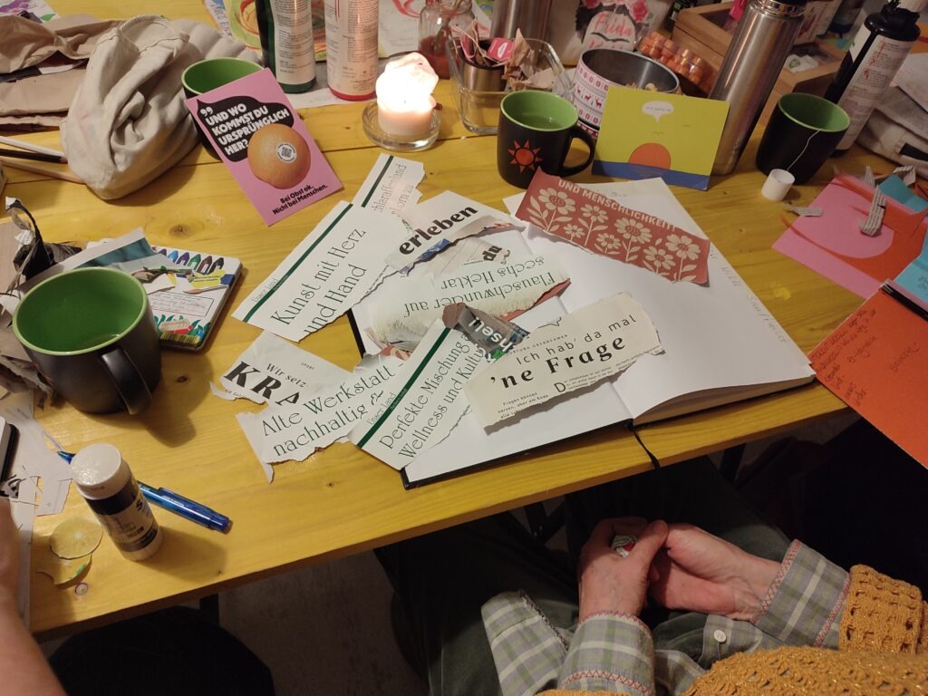 Zentral ist der gelbe Tisch des Büros von EinsWeiter. Auf diesem Tisch sind Zeitungen, Bastelmaterial, Pinsel und Farben.