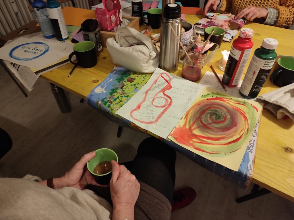 Zentral ist der gelbe Tisch des Büros von EinsWeiter. Auf diesem Tisch sind Zeitungen, Bastelmaterial, Pinsel und Farben. Außerdem liegen auf dem Tisch noch nicht fertig gestellte Collagen.