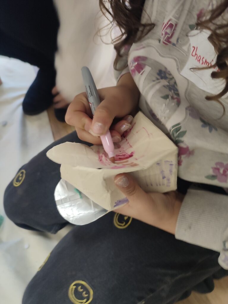 Ein Kind malt auf ein Blatt Papier mit einem roten Stift. Das Gesicht des Kindes ist nicht zu sehen.