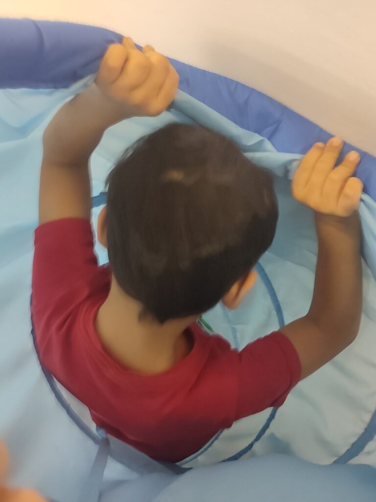 Ein Kind spielt in einem blauen Stofftunnel. Das Kind ist nur von hinten zu sehen.