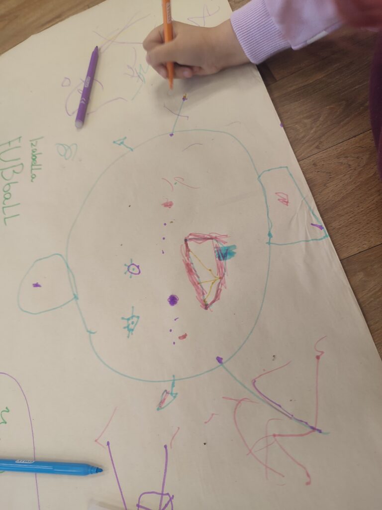 Das Foto zeigt die Hand von einem Kind. Es malt mit verschiedenen Farben auf ein Blatt Papier.