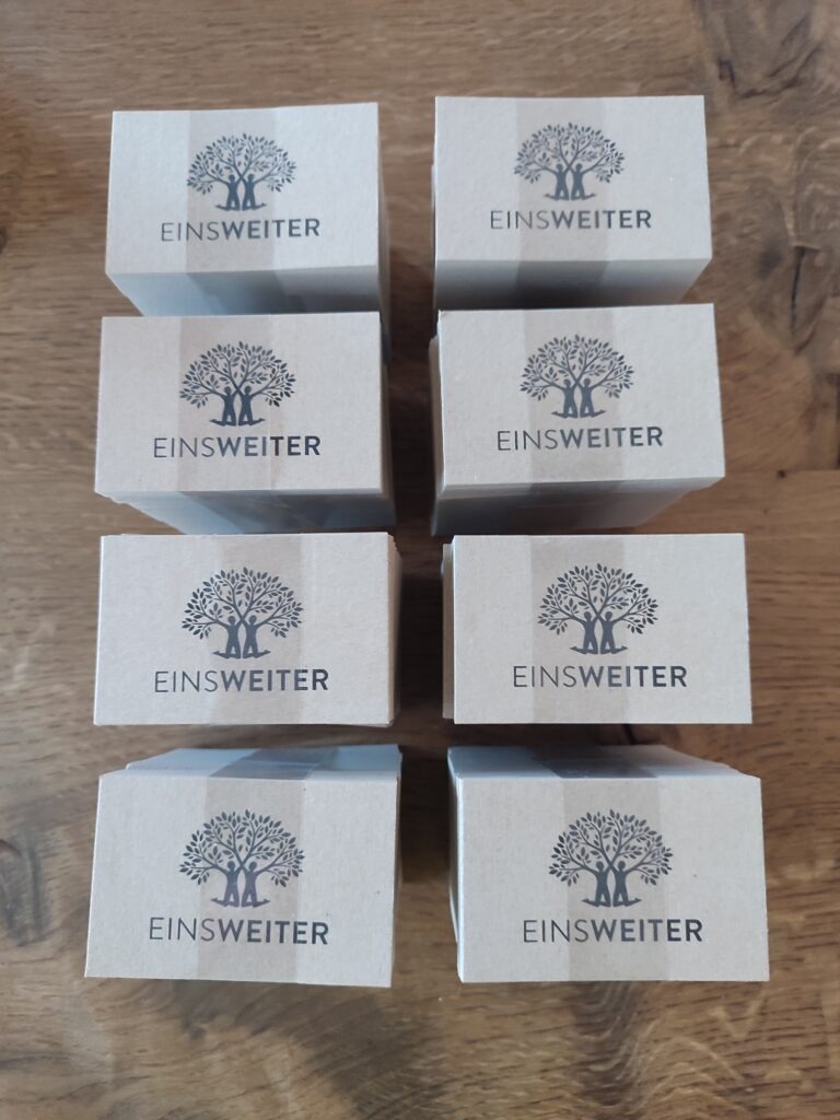 Das Foto zeigt mehrere Stapel der neuen Visitenkarten von EinsWeiter e.v., die auf einem Holztisch liegen. 