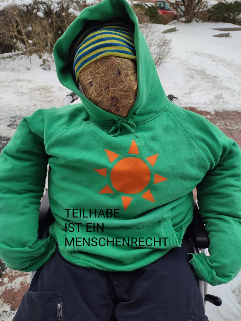 Eine Strohpuppe mit grünen Anti-Atomkraft Pullover sitzt im Rolli. Darauf steht: Teilhabe ist ein Menschenrecht. 
