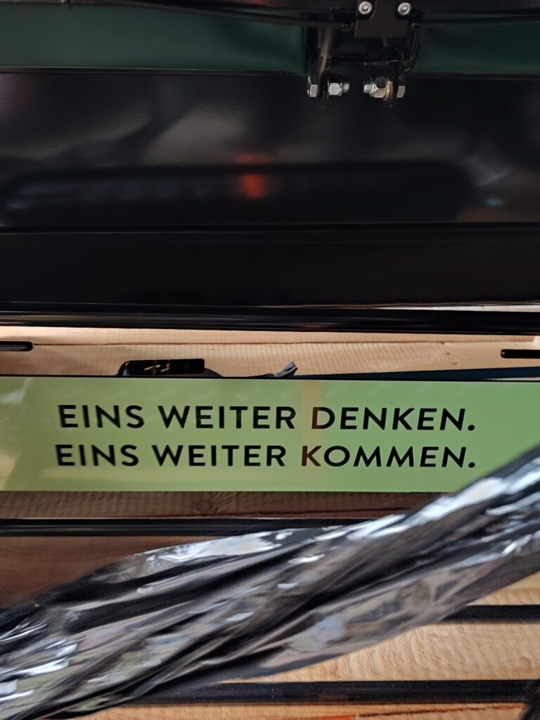 Das Bild zeigt einen vorderen Teil der Fahrradrikscha. Auf einer grün unterlegten Fläche stehen die Worte: Eins Weiter denken. Eins Weiter kommen.
